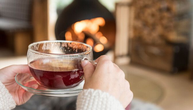 Frau trinkt gemütliche Tasse Früchtetee vor Kamin in Luxuslodge