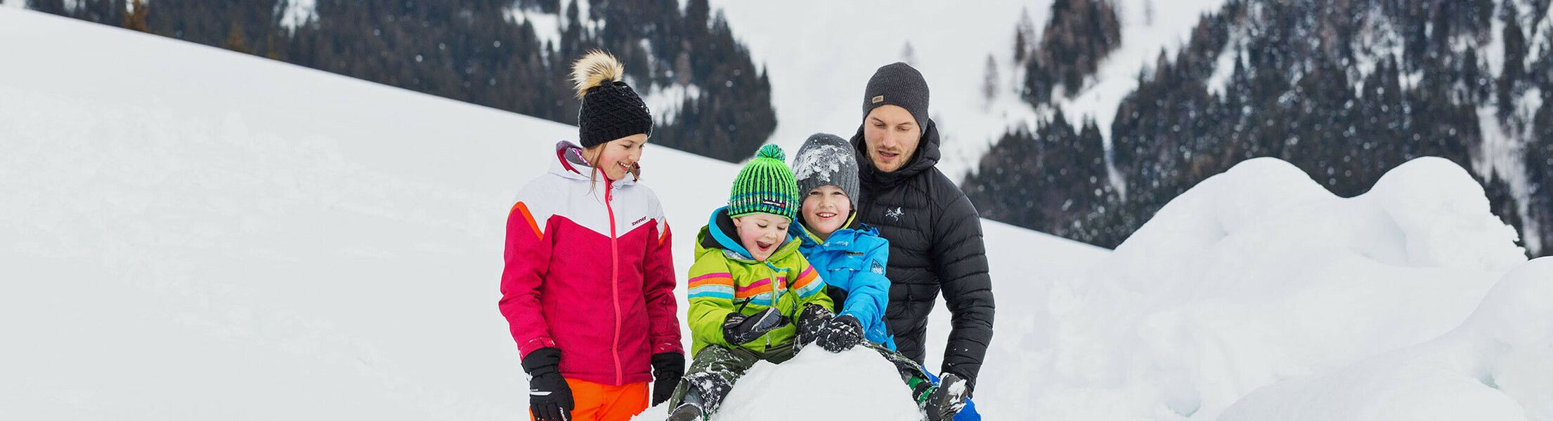 Familie baut Schneemann im Winter im Salzburger Land