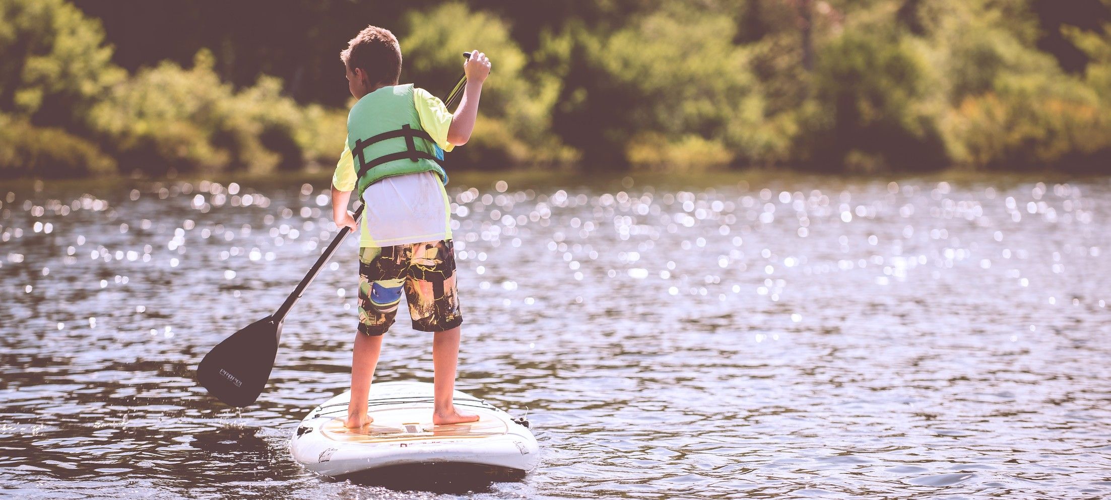 Kind steht auf Stand-Up Paddle im Wasser