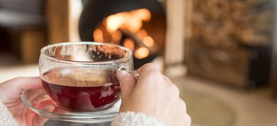 Frau trinkt gemütliche Tasse Früchtetee vor Kamin in Luxuslodge